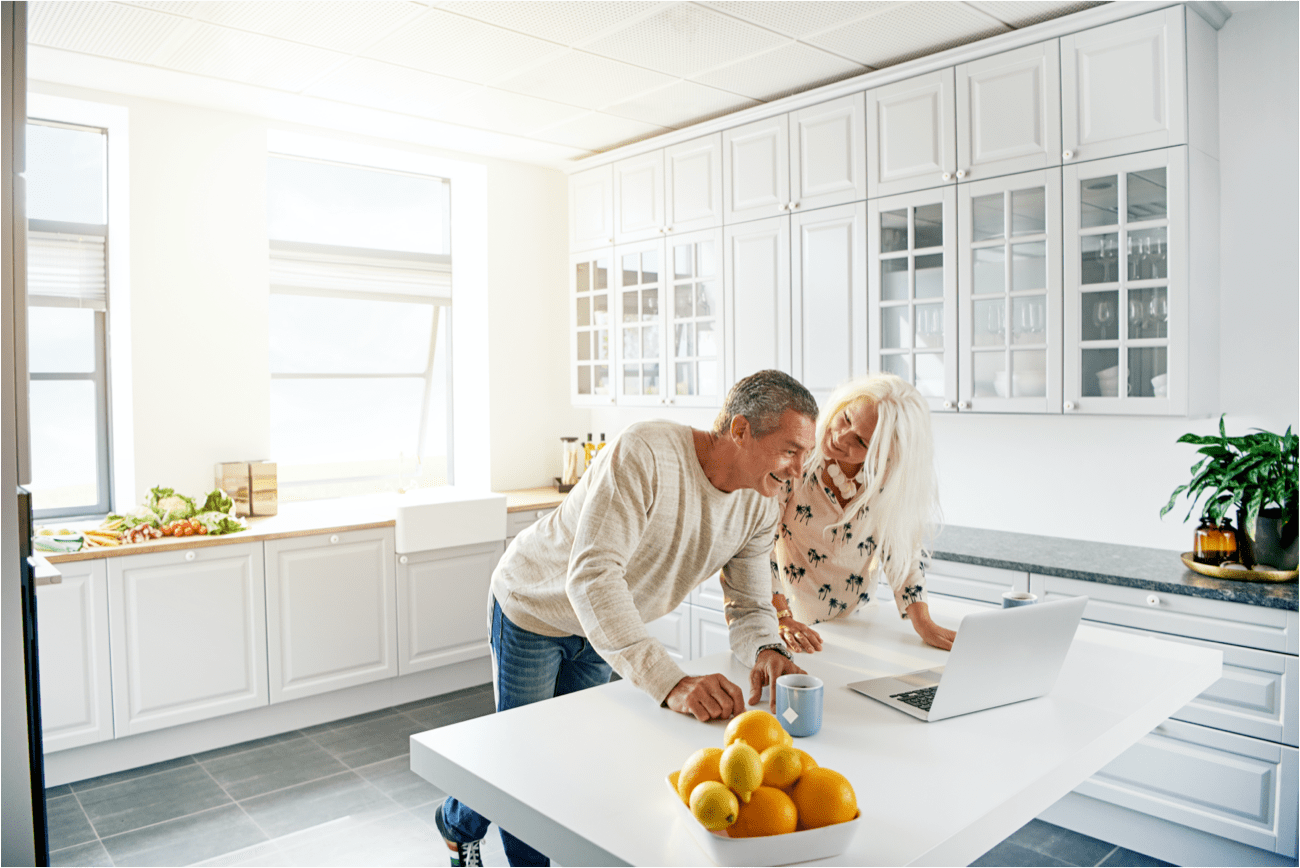 A couple is leaning over a laptop in a well lit kitchen.